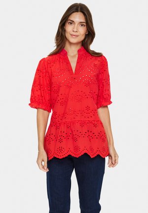 Red cotton blouse with short puff sleeves, eyelet pattern, and scalloped hem. Features a v-neck and gathered waist for a loose fit.