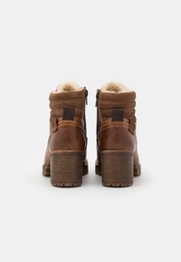 Bottines en cuir marron avec une doublure en fourrure douce, des talons en bois épais et des fermetures éclair sur les côtés. Présente une texture matelassée sur la partie supérieure.