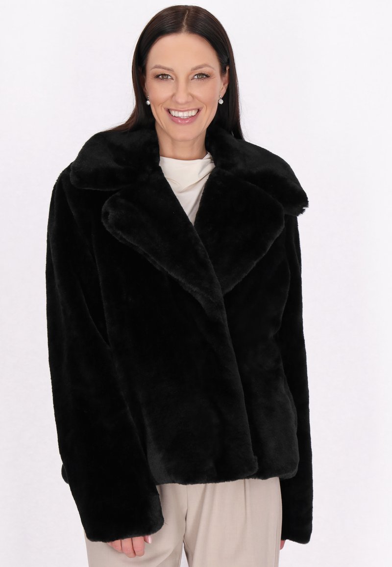 Sort faux fur-jakke med bred krave, lange ærmer og en afslappet pasform. Blød tekstur med en glat overflade, ingen synlig hardware eller mønstre.