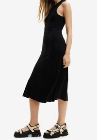 Musta ribbikankainen mekko, jossa istuva yläosa ja liehuva helma. Yhdistetty massiivisiin beige-mustiin sandaaleihin, joissa on useita hihnoja ja solkia.