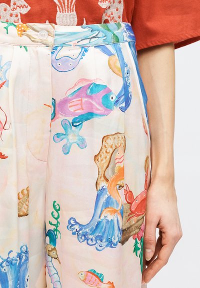 Pantalon taille haute avec des illustrations colorées sur le thème sous-marin, incluant des poissons, un crabe, un hippocampe et du corail, assorti à une chemise couleur rouille.