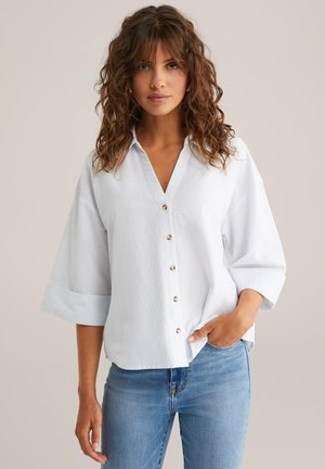 Camicia abbottonata a righe verticali blu chiaro e bianche, con colletto a punta, maniche larghe e bottoni dorati. Fit casual.