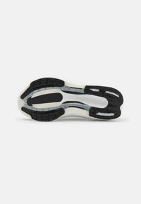 Semelle de chaussure de sport en noir et blanc avec une semelle extérieure en caoutchouc texturé, des rainures, une semelle intermédiaire en EVA et un détail en relief "LIGHTBOOST".