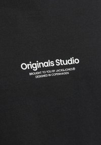 Svart t-shirt med vit text som läser "Originals Studio," "Brought to you by JACK&JONES," och "Designed in Copenhagen." Slät textur.