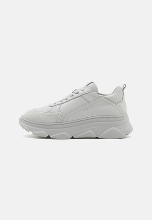 White leather sneaker with suede accents, thick rubber sole, textured panels, lace-up front, and logo detail on the side.