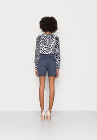 Navy shorts and a white blouse with a black leopard print. The blouse has long sleeves, while the shorts are tailored with back pockets.