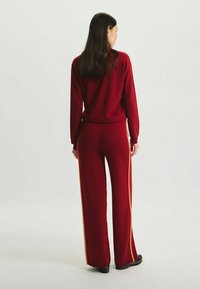 Pull en tricot rouge et pantalon large assorti avec des bandes latérales orange, présentant une coupe décontractée et des poignets et une taille côtelés.
