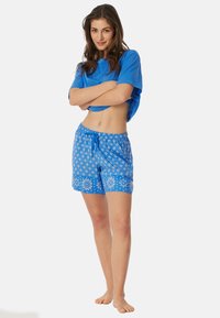 Blaues Baumwoll-T-Shirt mit kurzen Ärmeln, kombiniert mit blauen gemusterten Shorts mit floralen Designs und einem verstellbaren Kordelzugbund.