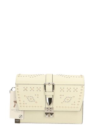 Sac à main en cuir crème avec des clous en métal, de forme rectangulaire, fermeture magnétique, détail de boucle décoratif et étiquette de marque attachée.