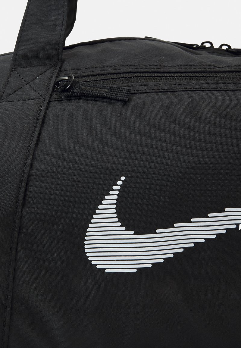 Bolsa de lona negra con un destacado logotipo blanco de Nike y rayas horizontales. Incluye un cierre con cremallera y asas resistentes.