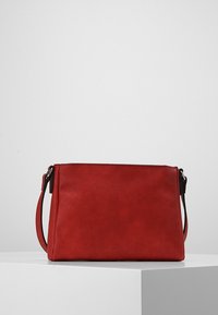 Czerwona torba na ramię z ekoskóry o prostokątnym kształcie, gładkiej fakturze i pojedynczym regulowanym pasku. Minimalistyczny design bez zdobień.