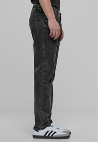 Mustad denim teksad sirge säärega, pleekinud tekstuuriga ja viie taskuga disainiga, kombineeritud valgete ja hallide tossudega, millel on mustad triibud.