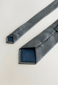 Krawatte aus gewebtem Stoff mit blauen und goldenen Mustern. Verfügt über eine glatte blaue Unterseite und quadratische Enden. Etikett auf einer Seite sichtbar.