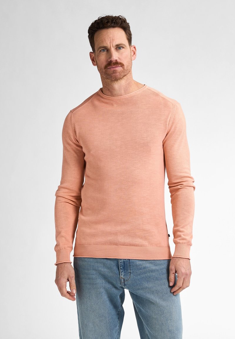 Rosa gerippter Langarm-Pullover mit Rundhalsausschnitt und schmalen Bündchen und Saum, getragen mit hellblauen Jeans. Glatte Textur mit subtilen Variationen.