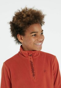 Pullover in pile arancione con colletto alto, mezza zip e dettaglio logo nero. Texture morbida, vestibilità casual e accenti di cucitura prominenti.