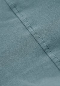 Textil i en mjuk, ljusblå färg med en slät yta och synlig sömnad längs sömmen.