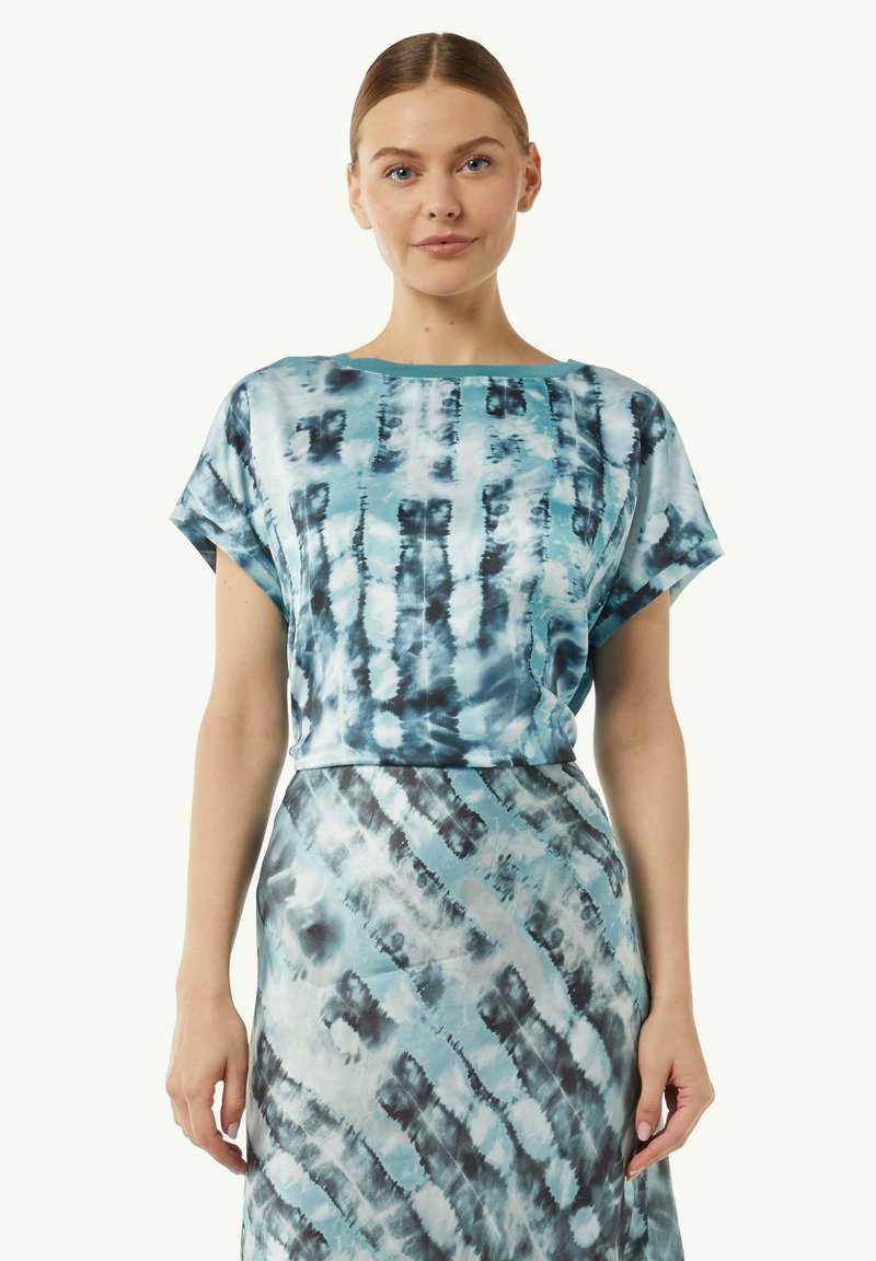 Niebieski top w stylu tie-dye o luźnym kroju i krótkich rękawach, z okrągłym dekoltem. Dobrany do spódnicy w tym samym stylu tie-dye. Gładka tekstura materiału.