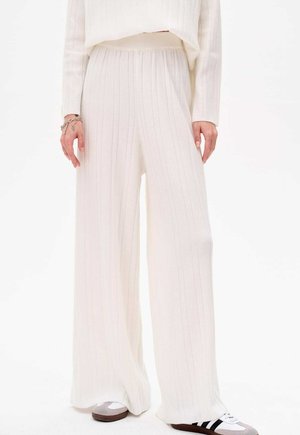 Weite Hosen aus geripptem weißen Strickstoff mit einem elastischen Bund. Das Outfit wird mit grau-weißen Sneakers kombiniert, die schwarze Streifen aufweisen.