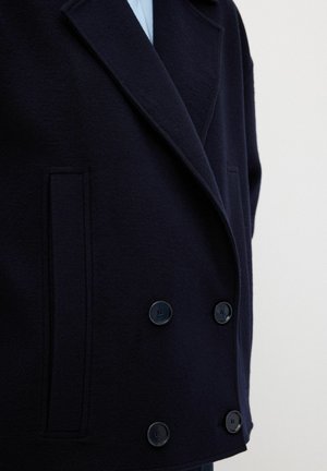 Marineblauer, doppelt gepuntertes Mantel aus weichem Wollstoff, mit großen schwarzen Knöpfen und zwei Seitentaschen, maßgeschneidert mit einem Reverskragen.