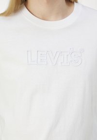 Balta medvilninė marškinėlių bluzonė su iškilniu "LEVI'S" logotipu tos pačios spalvos. Klasikinio apvalaus kaklo dizainas su trumparankoviais. Švelni tekstūra.