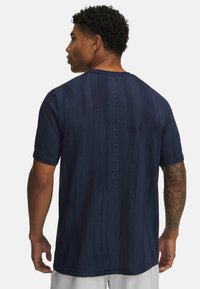 Mørkeblå kortærmet atletisk T-shirt med et struktureret mønster og "UNDER ARMOUR"-logo langs ryggen. Letvægts, åndbart materiale.