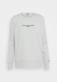 Sweatshirt gris clair à col rond, avec un logo noir horizontal et de petites touches de couleur sur les poignets et le col.