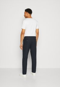 Navy trousers with a tailored fit, made of lightweight fabric, featuring two back pockets with buttons and paired with a white T-shirt.