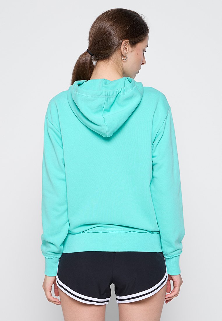 Felpa verde menta con cappuccio regolabile, polsini e fondo a coste. Abbinata a pantaloni sportivi neri con strisce bianche decorative.