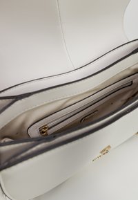 Interno di una borsa a tracolla in pelle bianca, caratterizzato da un ampio scomparto principale con una tasca con cerniera, foderato in beige e con dettagli in metallo dorato.