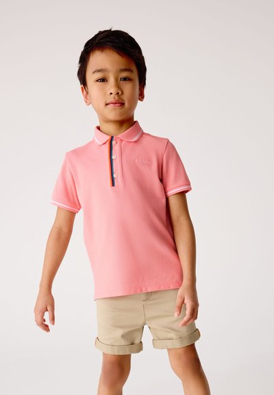 Roze poloshirt met een geribbelde kraag, een knoopsluiting met drie knopen en een contrasterend gestreept detail. Gecombineerd met opgerolde beige shorts.