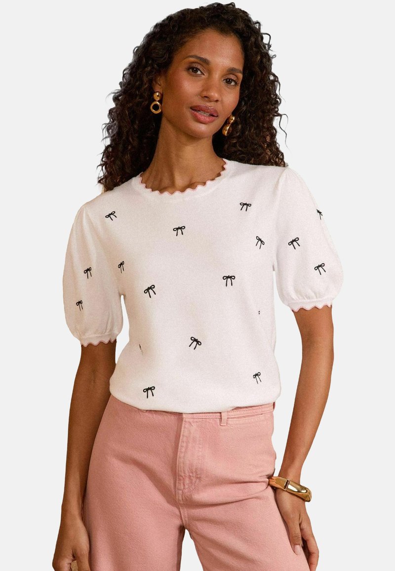 Balts īsām piedurknēm zeķubikšu ar melnu loku izšuvumu un viļņotu kakla izgriezumu, apvienots ar gaiši rozā biksēm. Viegla un gluda tekstūra.