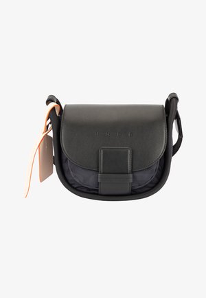 Bolso bandolera compacto negro con cierre de solapa, correa ajustable y etiqueta beige claro en el lado izquierdo.