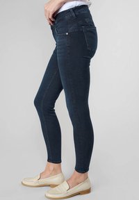 Jeans skinny bleu foncé en denim extensible, avec une taille mi-haute, un design à cinq poches et un léger délavage le long des coutures extérieures.