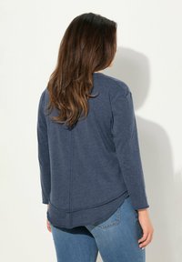 Dunkelblauses langärmeliges Hemd mit abgerundetem Saum und strukturiertem Finish. Die Rückseite weist gestickte Details und eine lockere Passform auf.