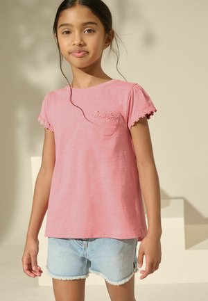 Lyserød bomulds t-shirt med korte puffærmer, dekorativ blomsterbroderi på lommen, samt parret med lyseblå denimshorts.