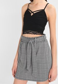 Top corto nero con pizzo e spalline sottili, abbinato a una gonna a fantasia checkered bianco e nero con vita alta e cintura con fiocco.