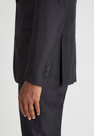 Granatowa marynarka o teksturowanym wykończeniu, z bocznym rozcięciem, trzema czarnymi guzikami na mankietach oraz wąskim krojem.