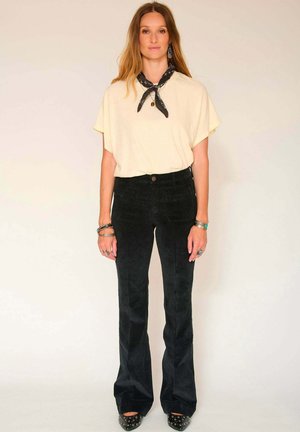 Top à manches courtes de couleur crème associé à un pantalon en velours côtelé noir taille haute à pattes d'éléphant et des chaussures noires à bout pointu avec des clous en argent.