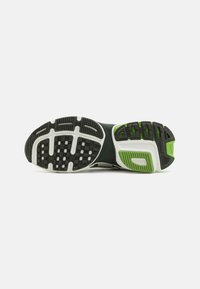 Suela de zapato con una superficie de goma negra con acentos verdes y patrones texturizados para tracción, bordeada por un acolchado blanco.