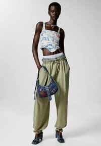 Top bianco corto con grafiche blu, pantaloni verde oliva a gamba stretta, borsa di jeans blu con borchie e sandali blu con tacco alto.