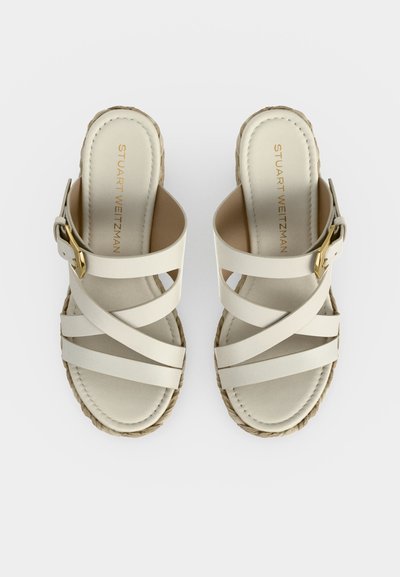 Sandales à enfiler en cuir beige avec de larges brides croisées, boucle dorée sur le côté, semelles intérieures rembourrées et semelles intermédiaires en corde tressée.