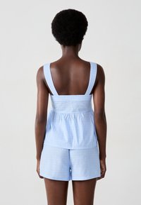 Canottiera in cotone blu chiaro con spalline larghe e corpino aderente, caratterizzata da punti texturizzati. Abbinata a pantaloni corti blu chiaro coordinati.