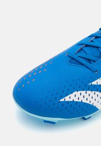 Chaussure de football bleue avec une tige synthétique texturée, présentant des accents orange et un logo blanc. Embout rond et lacets plats. Semelle à crampons.