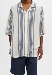 Camicia a maniche corte con bottoni di un leggero beige con righe verticali blu. Presenta un colletto all'italiana e una vestibilità rilassata. Realizzata in tessuto testurizzato.