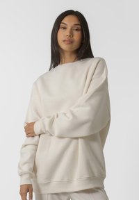 Helebeežist suuruses dressipluus ümmarguse kaelusega ja soonikkoes varrukatega. Omab minimaalset brändingut rinna piirkonnas. Pehme, tekstureeritud kangas.