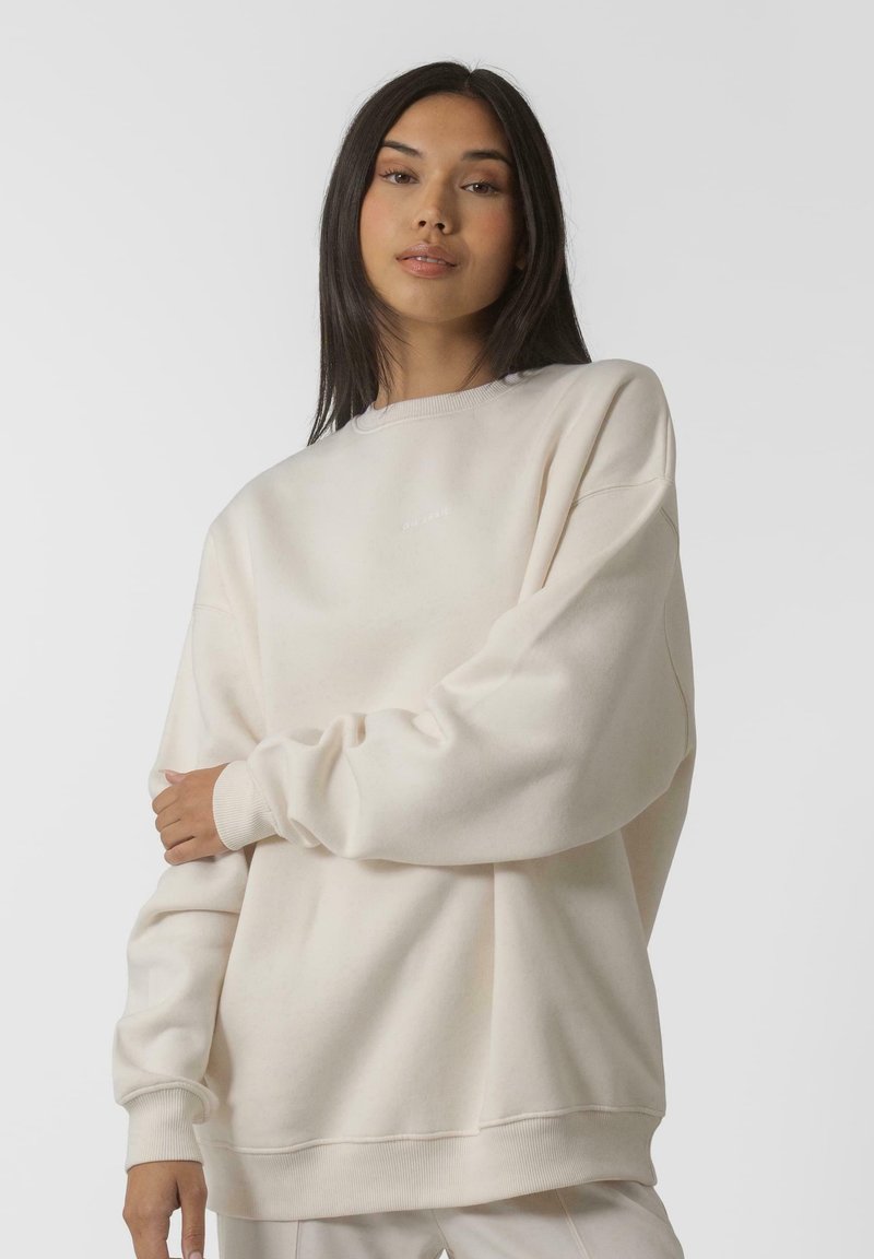 Helebeežist suuruses dressipluus ümmarguse kaelusega ja soonikkoes varrukatega. Omab minimaalset brändingut rinna piirkonnas. Pehme, tekstureeritud kangas.