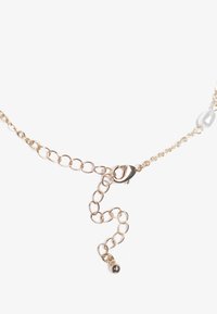 Collier en chaîne dorée avec des maillons ovales, comportant un fermoir et une chaîne allongée avec une petite perle ronde à l'extrémité. Texture lisse, design minimal.