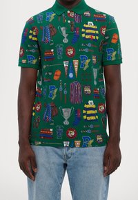 Zielona koszulka polo z różnorodnymi kolorowymi wzorami, w tym elementami sportowymi, krawatami i trofeami. Miękka tkanina, klasyczny kołnierzyk.