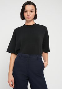 Μαύρο πουκάμισο σε υπερμεγέθη γραμμή με κοντά μανίκια και στρογγυλή λαιμόκοψη, σε συνδυασμό με μπλε σκούρο παντελόνι σε κομμένη γραμμή. Ομαλή υφή, μινιμαλιστικός σχεδιασμός.