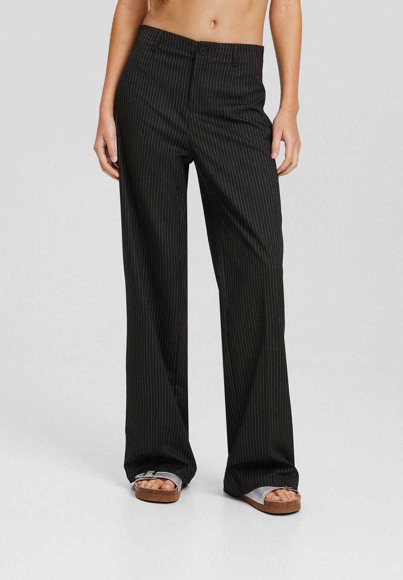 Pantalon noir à rayures avec une coupe décontractée, doté d'une fermeture à boutons et de jambes larges. Texture lisse et design ajusté avec des rayures verticales.